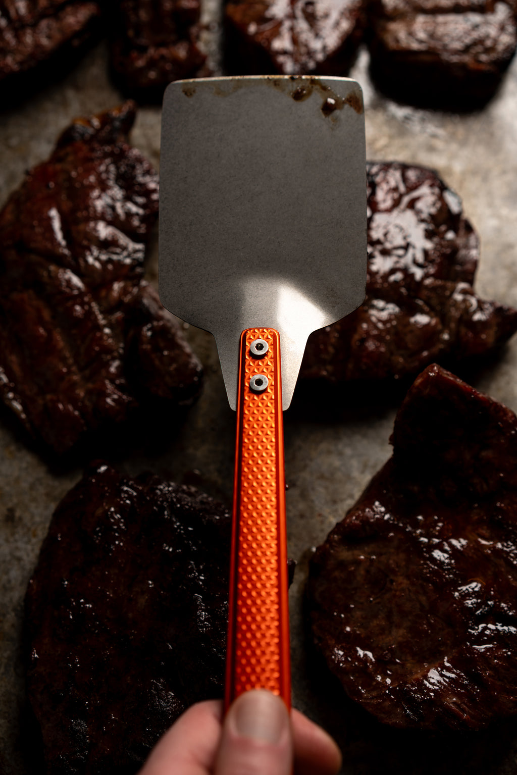 orange millrite spatula in hand above meat behind