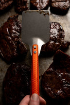 orange millrite spatula in hand above meat behind