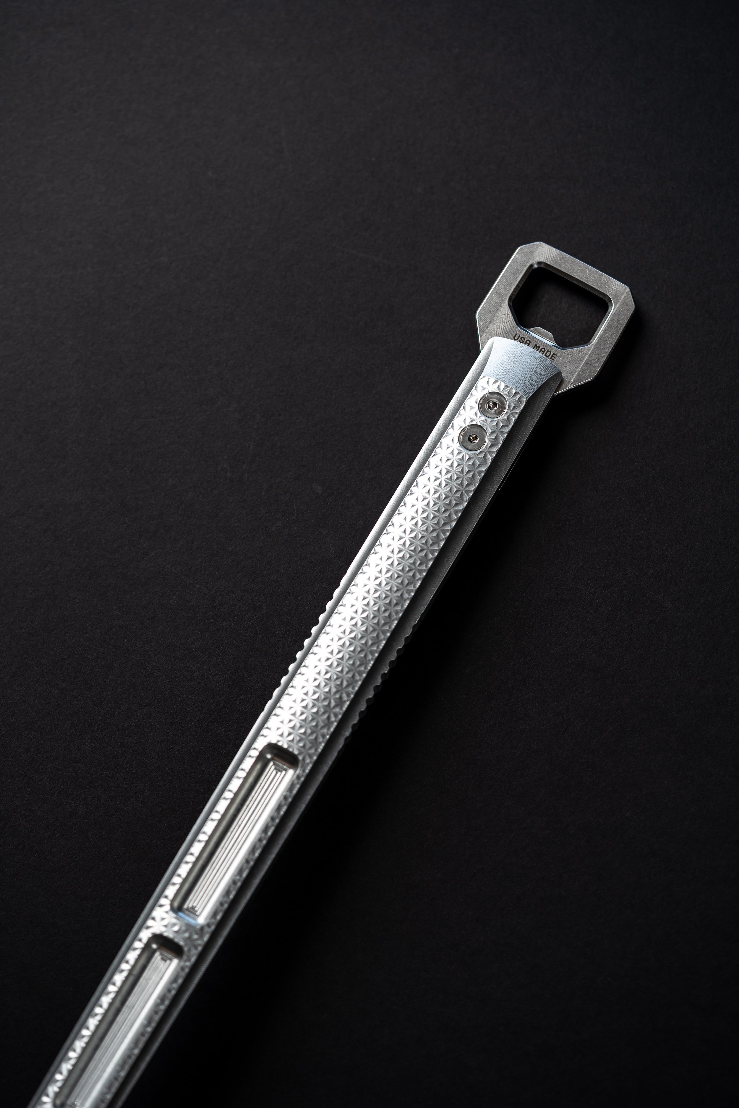 Silver spatula with attached bottle opener photographed on black background.