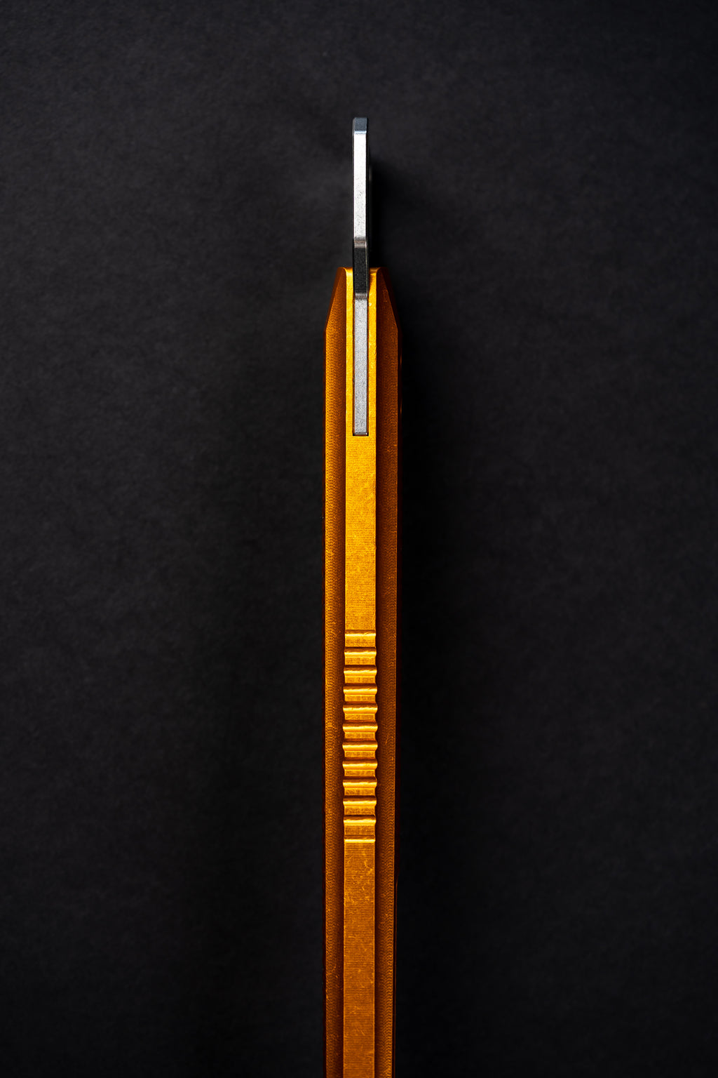 A close-up of a metallic gold and silver tool or accessory with a ribbed textured body, standing vertically against a dark black background.