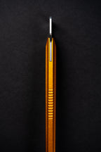 A close-up of a metallic gold and silver tool or accessory with a ribbed textured body, standing vertically against a dark black background.