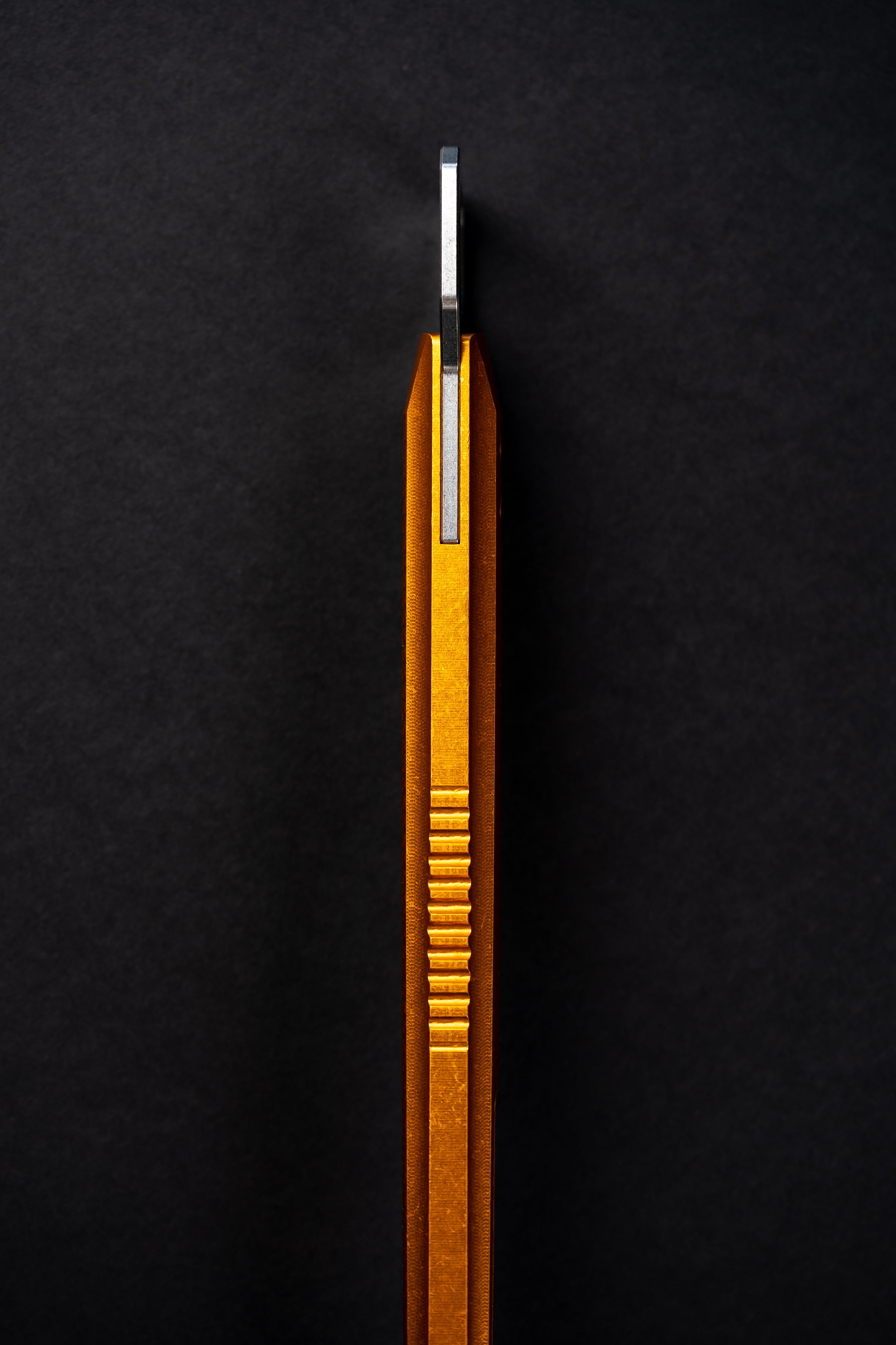 A close-up of a metallic gold and silver tool or accessory with a ribbed textured body, standing vertically against a dark black background.